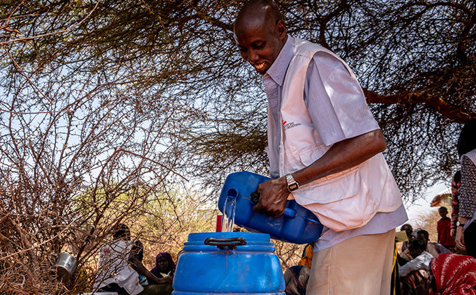 Un employé de MSF verse de l’eau dans un bidon bleu.