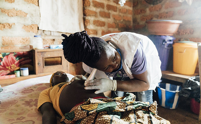 Une employée de MSF ausculte une femme enceinte allongée sur son lit au moyen d’un stéthoscope en forme de cône placé sur le ventre de la patiente.