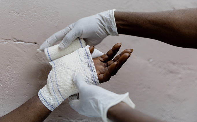 Une personne portant des gants médicaux bande le poignet et la main d’une patiente.