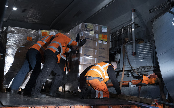 Trois personnes déplacent une palette de boîtes dans un camion de livraison.