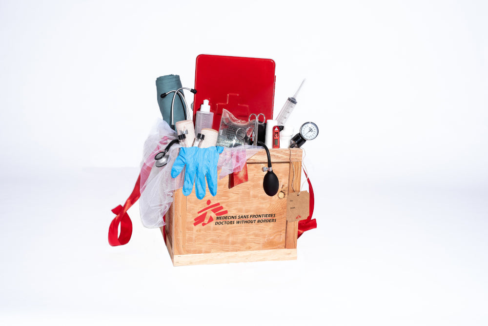 Une caisse en bois regorge d’articles utilisés par MSF, comme un stéthoscope, un gilet de sauvetage, des instruments chirurgicaux, une couverture, un thermomètre, un mégaphone et des bottes en caoutchouc.