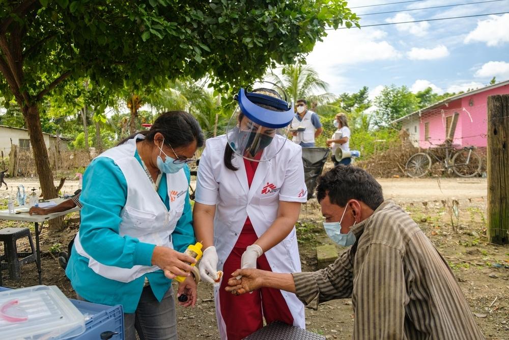 Des membres de MSF portant des masques chirurgicaux désinfectent le doigt d’un patient portant un masque chirurgical.