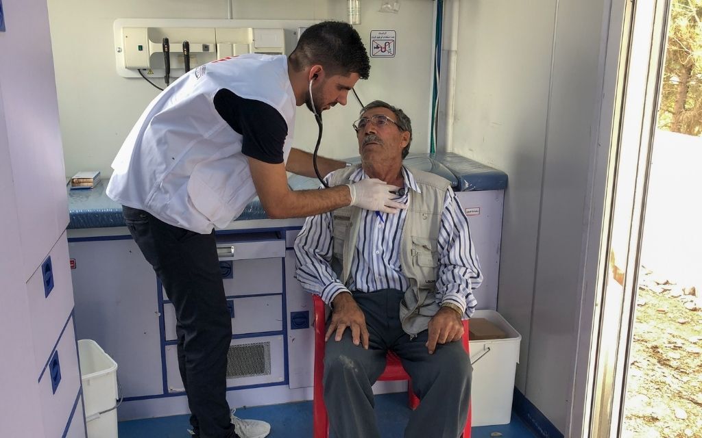 Un agent de santé ausculte à l’aide d’un stéthoscope le thorax d’un homme âgé assis sur une chaise.
