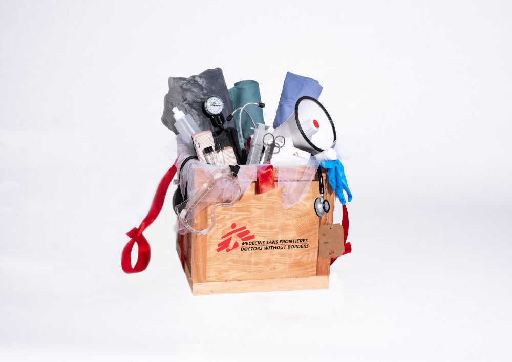 Une caisse en bois regorge d’articles utilisés par MSF, comme un stéthoscope, un gilet de sauvetage, des instruments chirurgicaux, une couverture, un thermomètre, un mégaphone et des bottes en caoutchouc.